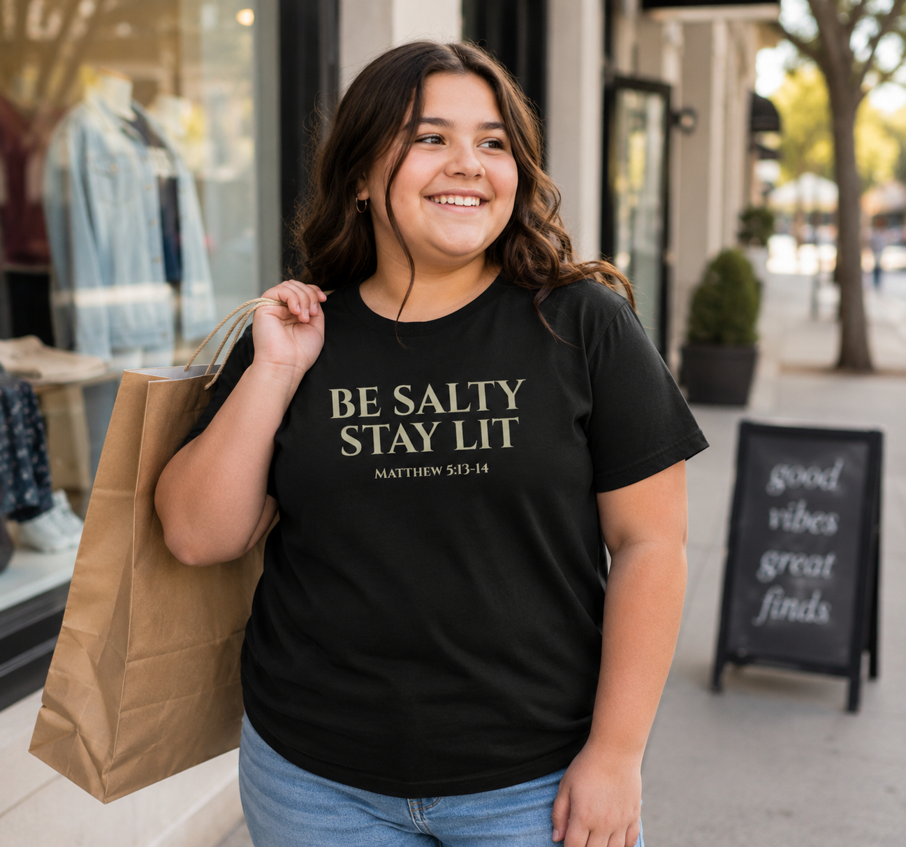 Plus size tween girl wearing a black “Be Salty Stay Lit” youth Christian t-shirt while shopping outdoors on a modern city sidewalk with a fun, youthful vibe.