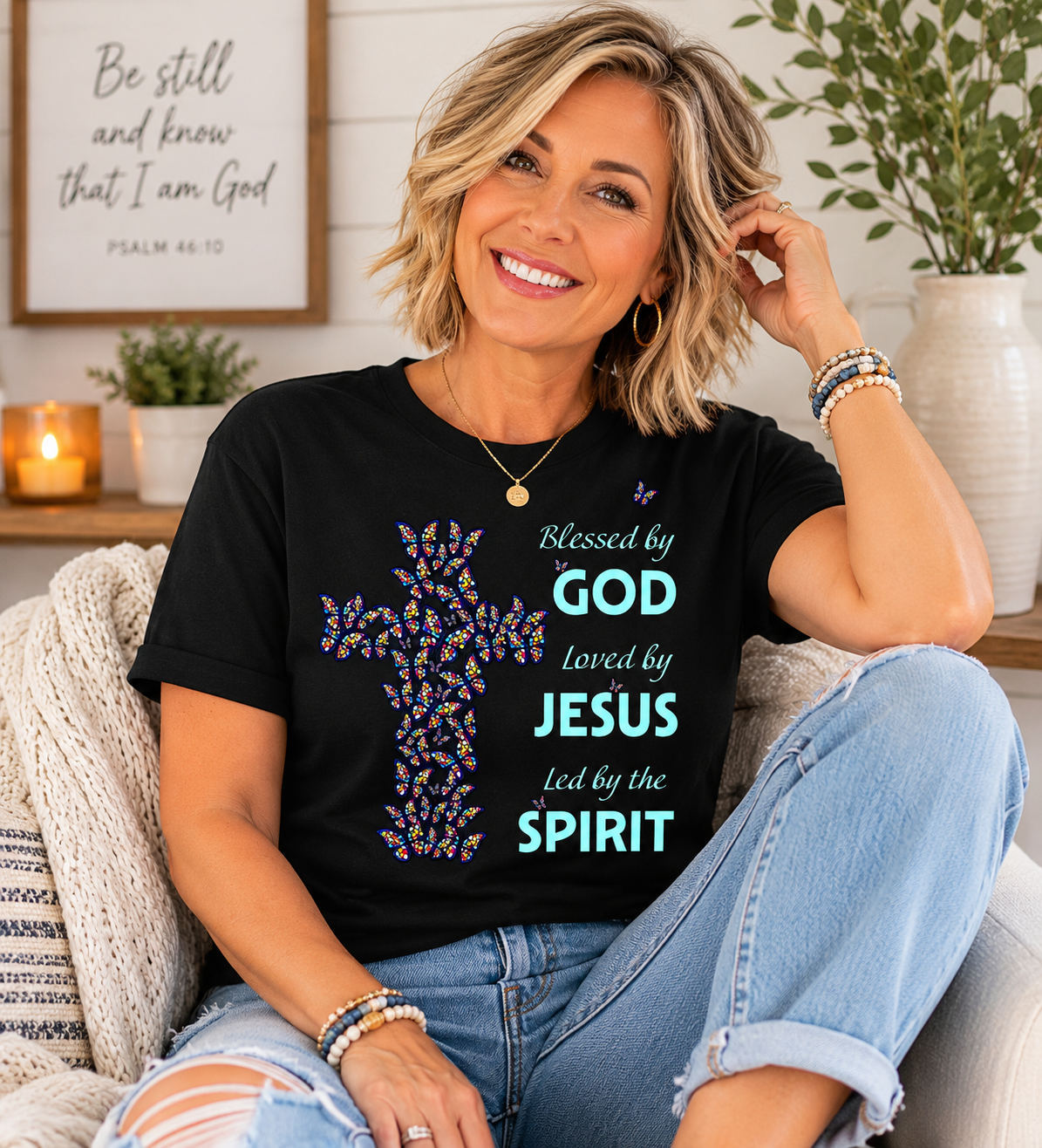 Woman with short blonde hair wearing black Christian butterfly cross t-shirt while relaxing in a cozy neutral-toned living room with soft natural lighting and modern farmhouse decor