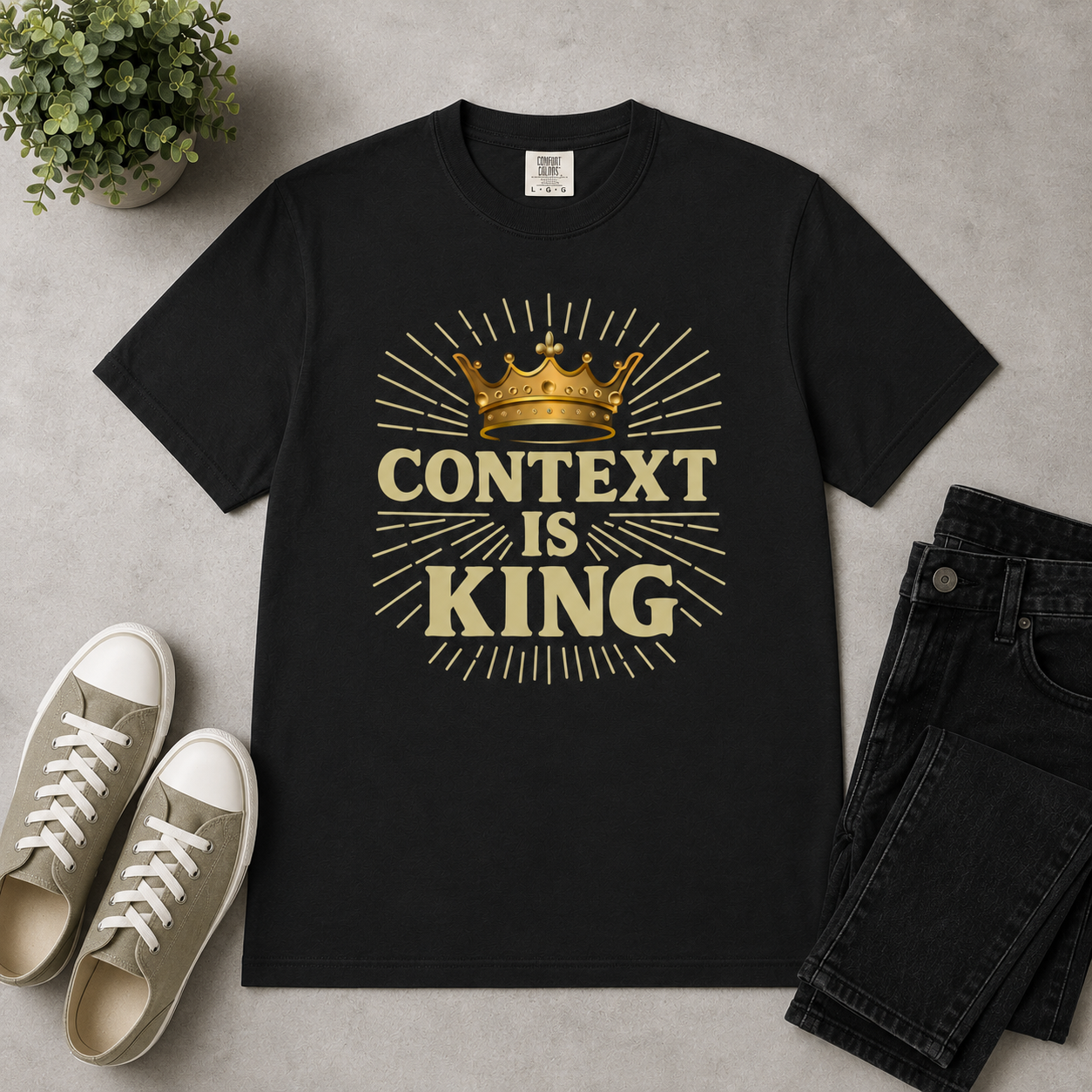 Black “Context Is King” Christian graphic t-shirt flat lay styled with hemp canvas sneakers, dark denim, a black notebook and pen, and modern neutral decor on a textured light gray background