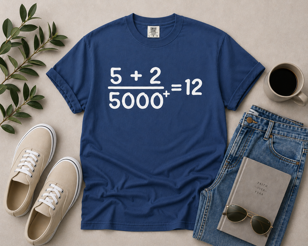 China blue Comfort Colors Christian graphic t-shirt flat lay featuring the “5 + 2 / 5000+ = 12” miracle equation design styled with light denim, neutral sneakers, coffee, and modern accessories.