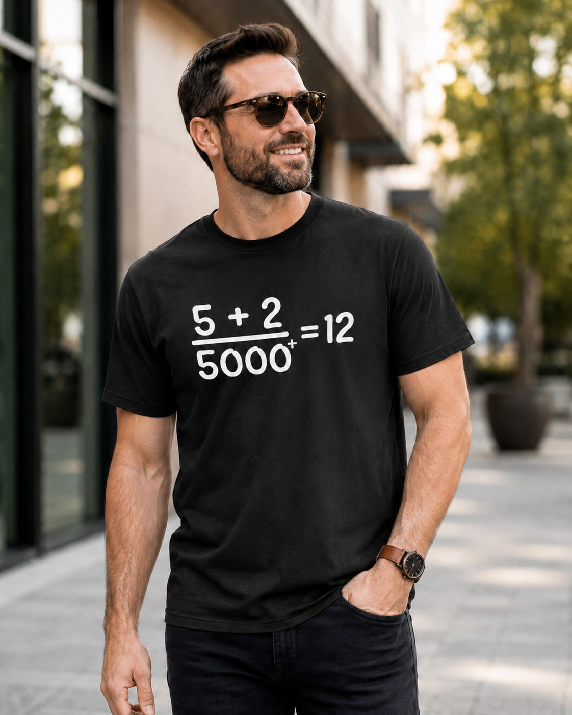Clean-cut man wearing a black Comfort Colors Christian math graphic t-shirt outdoors in a modern city setting featuring the “5 + 2 / 5000+ = 12” miracle design in white print.