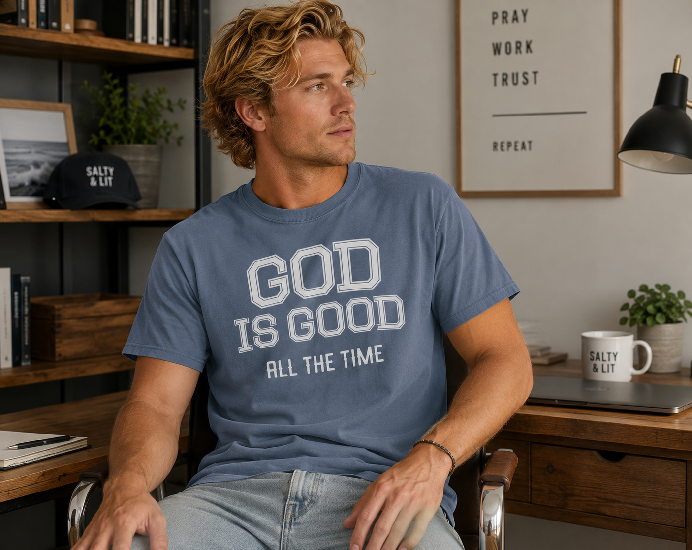 Man wearing the God Is Good All The Time Christian t-shirt in Blue Jean Comfort Colors 1717 while seated in a modern home office workspace.