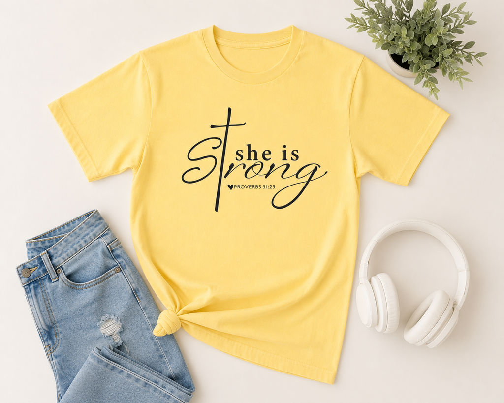 Flat lay mockup of a butter yellow “She is Strong” Christian youth t-shirt styled with light denim jeans, white wireless headphones, and neutral modern accessories.