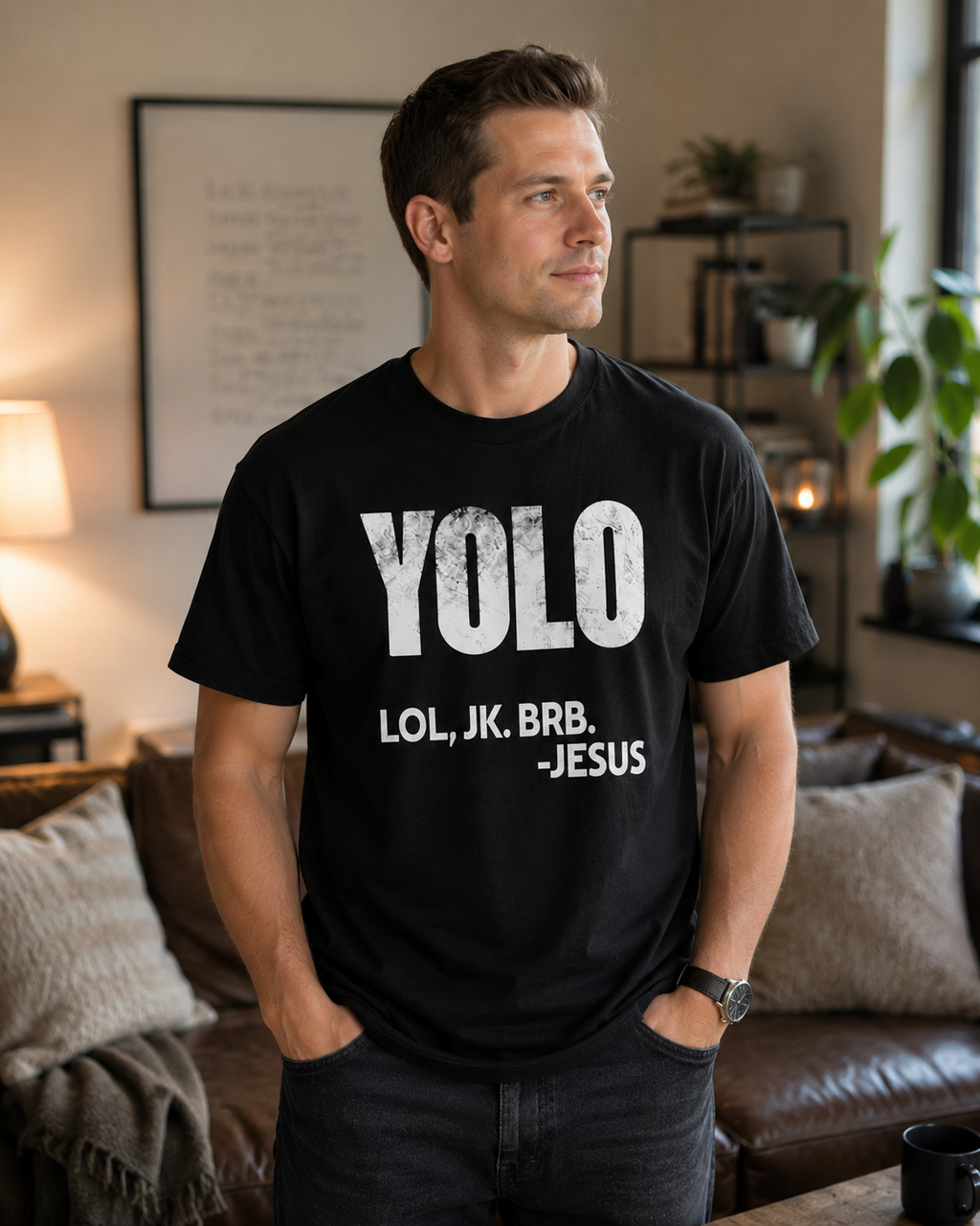 Clean-cut man in his 30s wearing black Christian humor t-shirt with “YOLO LOL, JK. BRB. -Jesus” graphic while standing in a cozy modern living room with warm natural lighting