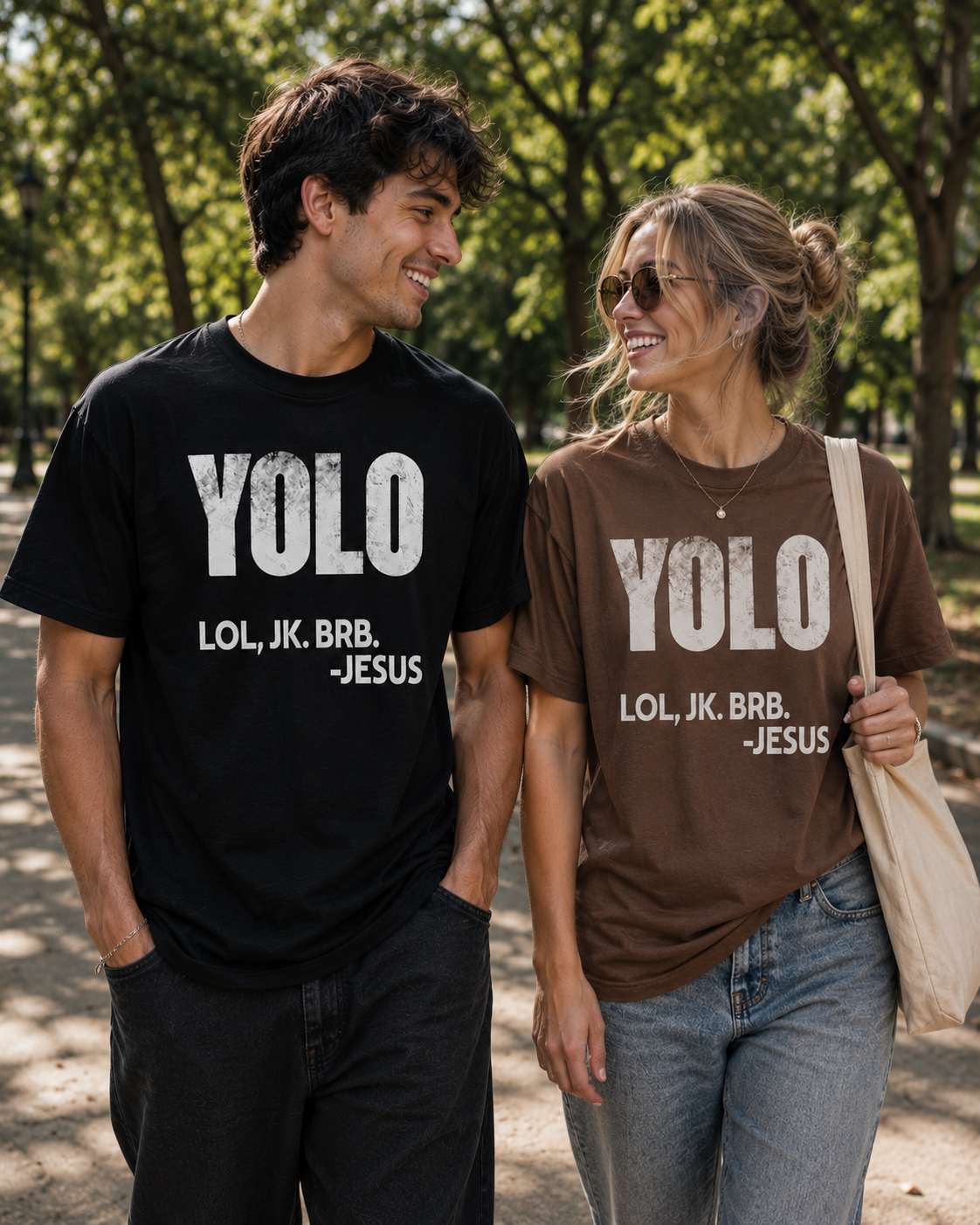 Young couple walking together in a sunny park wearing matching Christian humor t-shirts, with the woman in an espresso brown “YOLO LOL, JK. BRB. -Jesus” shirt and the man in a black version of the design