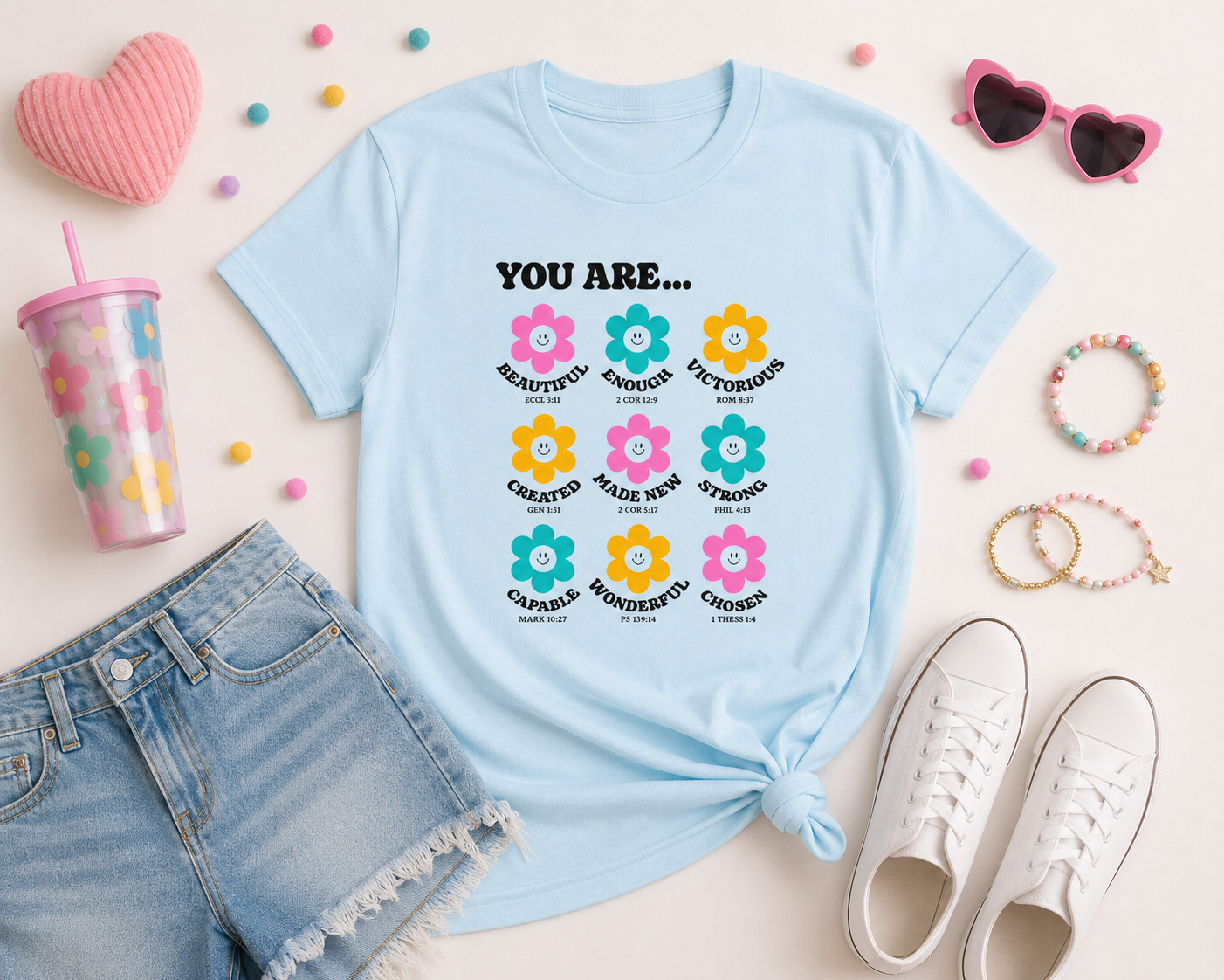 Flat lay mockup of a chambray blue “You Are…” Christian youth graphic t-shirt styled with denim shorts, white sneakers, colorful accessories, and modern playful decor in a bright youthful aesthetic.